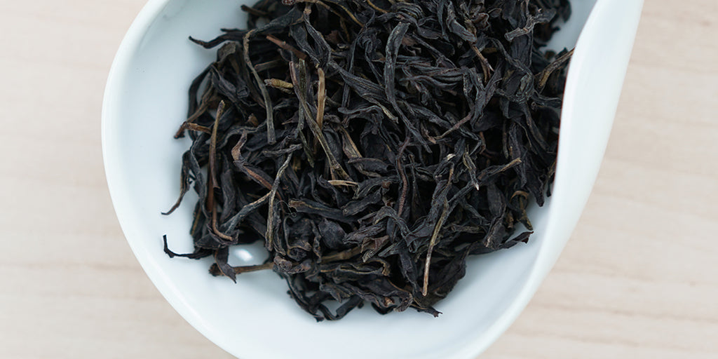 A white dish containing dry Phoenix oolong tea leaves.