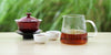 From left to right, a gaiwan, two teacups, and a glass server. The teacups and server have Aged Tieguanyin tea in them.