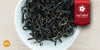 A white dish containing dry black tea leaves. A red ribbon in the top right corner reads “Red Label Collection”, and an orange circle in the bottom left corner reads "MX"