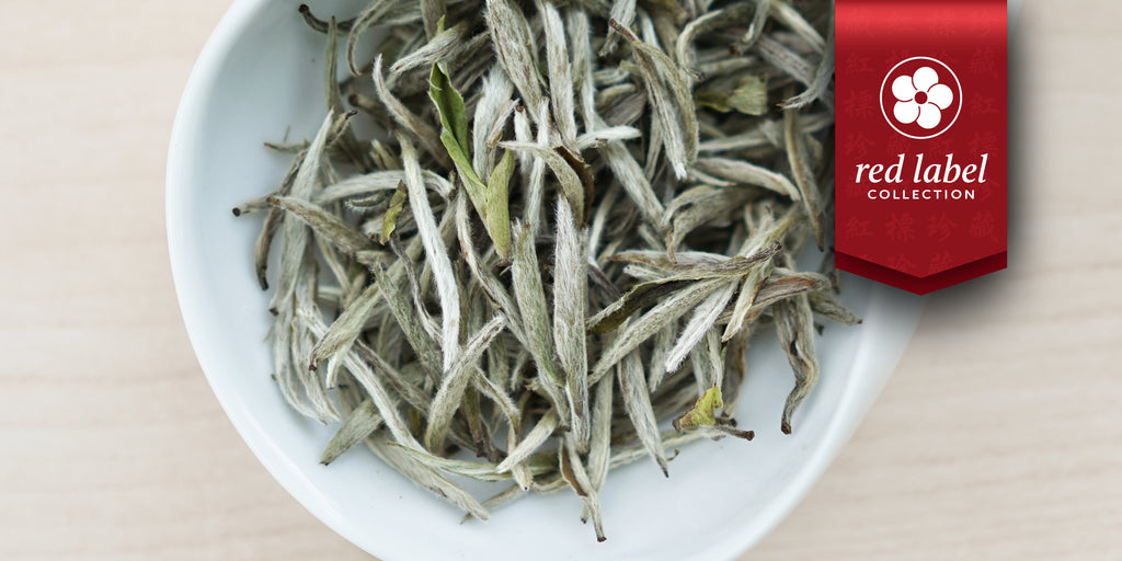 A white dish containing dry white tea leaves. A red ribbon in the top right corner reads “Red Label Collection”