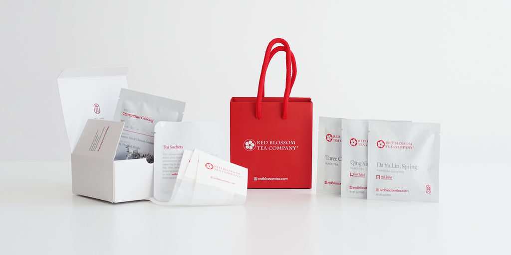 A party favor kit consisting of a red gift bag, a white mini gift box, and several tea sachets, and four samples of tea displayed on a white background.