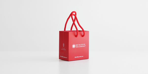 A small red bag with Red Blossom Tea Company's logo on it in reflective silver.