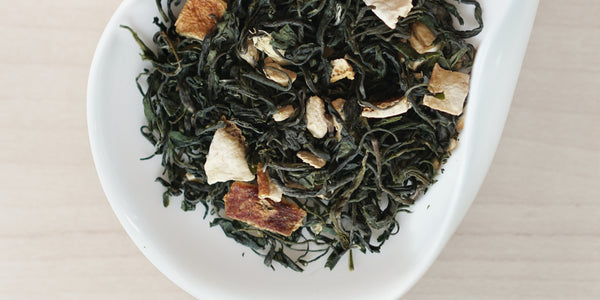 A white dish containing dry green tea leaves, dried orange peel, and ginger.