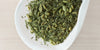 A white dish containing dry green tea leaves, toasted rice, and matcha powder.