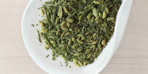 A white dish containing dry green tea leaves, toasted rice, and matcha powder.