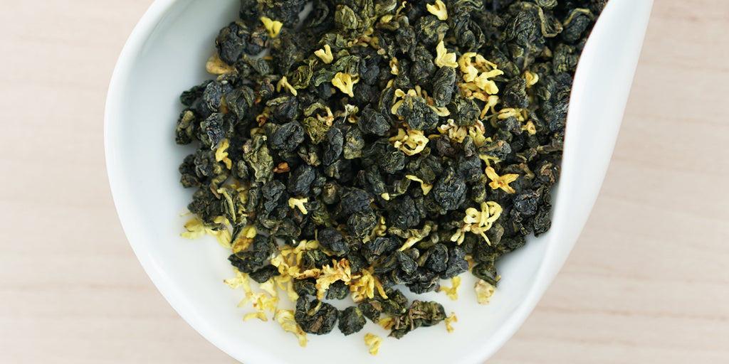 A white dish containing dry Formosa oolong tea leaves and yellow osmanthus flowers.