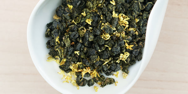 A white dish containing dry Formosa oolong tea leaves and yellow osmanthus flowers.