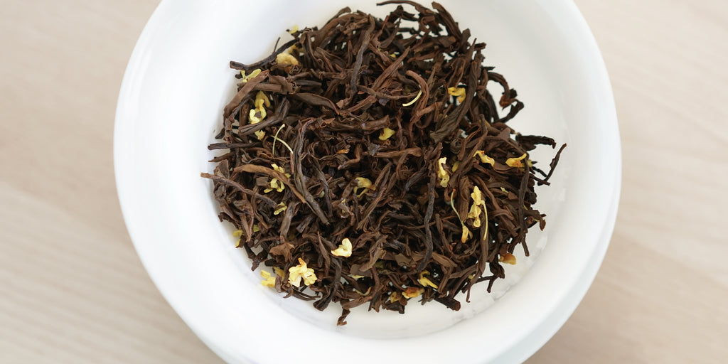 A top-down photo of brewed black tea leaves and yellow osmanthus flowers in a gaiwan.