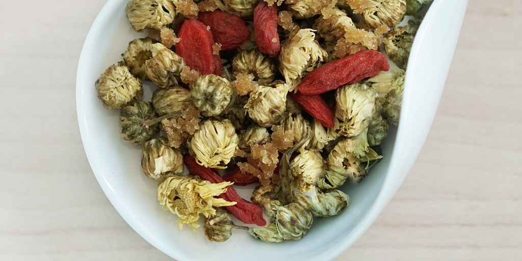 A white dish containing dry chrysanthemum buds, goji berries, and winter melon sugar.