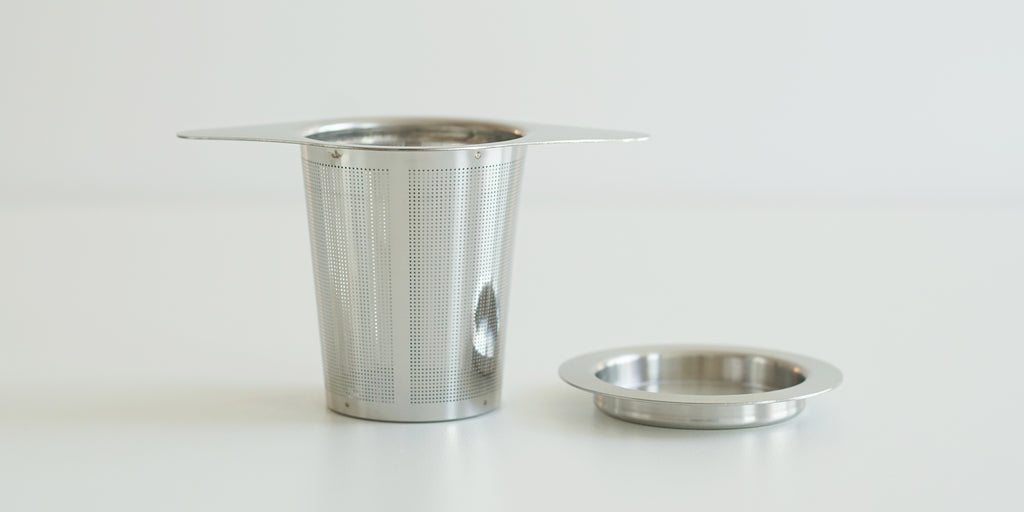 Side view of a steel infuser basket, with wings to hang over the top of a cup. A steel lid is set off to the side.