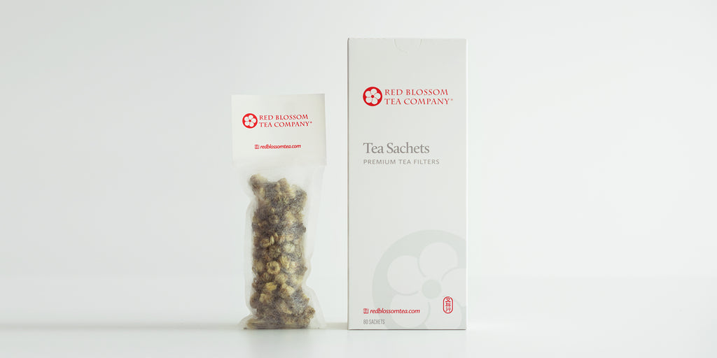 A tea sachet filled with chrysanthemum buds next to a box of tea sachets.