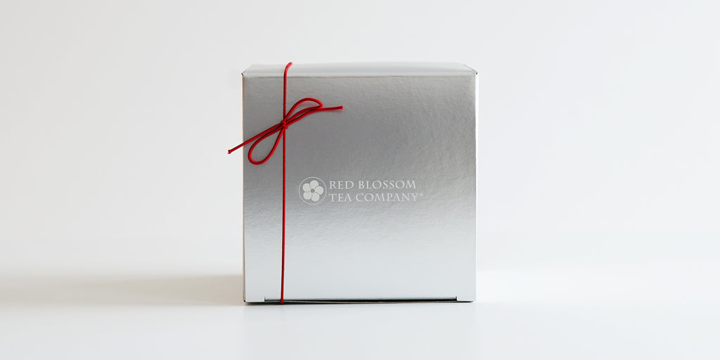 A silver box with a white logo in the middle and a red bow in the top left corner.