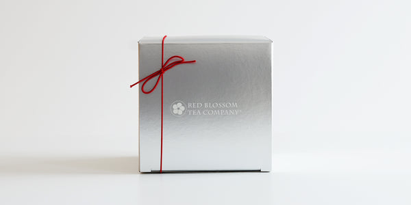 A silver box with a white logo in the middle and a red bow in the top left corner.