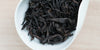 A white dish containing dry Wuyi oolong tea leaves.