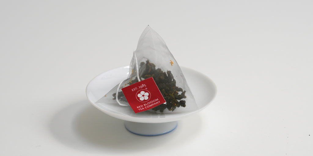 A triangular tea bag with a red label sits on a small white dish.