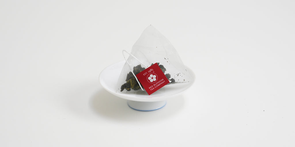 A triangular tea bag with a red label sits on a white dish.