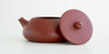 Side view of a terracotta-colored yixing teapot. The lid is facing the camera, resting against the handle.