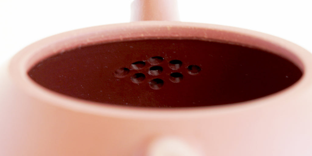 Rear view of the inside of a terracotta-colored yixing pot, showcasing the built-in filter made by punching small holes in the clay.