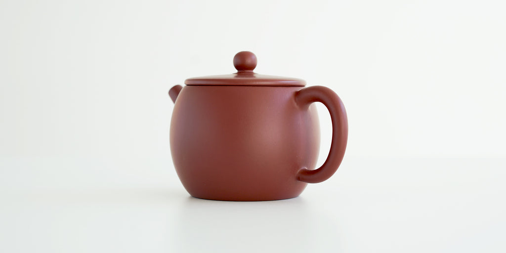 Rear view of a terracotta-colored yixing pot, highlighting the thin handle.