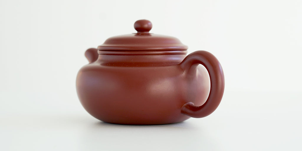 Rear view of a terracotta-colored yixing pot, highlighting the rounded handle.