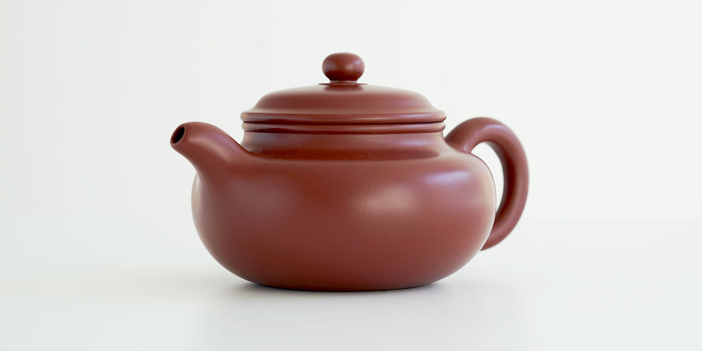 Front view of a terracotta-colored yixing pot highlighting the curved spout.