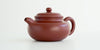 Front view of a terracotta-colored yixing pot highlighting the curved spout.