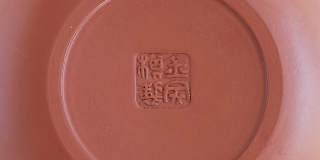 The bottom of a terracotta-colored yixing teapot. A maker’s mark is stamped into the base.