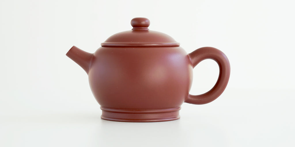 Side view of a terracotta-colored yixing pot, highlighting the round shape with rings around it.