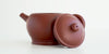 Side view of a terracotta-colored yixing teapot. The lid is facing the camera, resting against the handle.