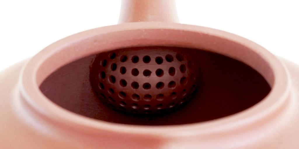 Rear view of the inside of a terracotta-colored yixing pot, showcasing the built-in filter made by punching small holes in the clay.