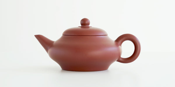 Side view of a terracotta-colored yixing pot, highlighting the smooth and flowing shape.
