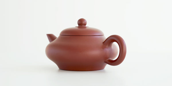 Rear view of a terracotta-colored yixing pot, highlighting the delicate handle.