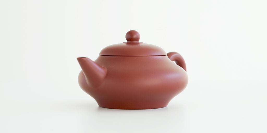Front view of a terracotta-colored yixing pot highlighting the angular spout.