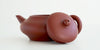 Side view of a terracotta-colored yixing teapot. The lid is facing the camera, resting against the handle.