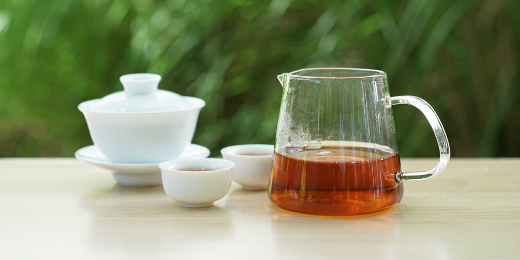 From left to right, a gaiwan, two teacups, and a glass server. The teacups and server have black tea in them.
