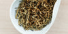 A white dish containing dry black tea leaves.