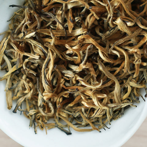 A white dish containing dry black tea leaves.