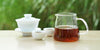 From left to right, a gaiwan, two teacups, and a glass server. The teacups and server have black tea in them.