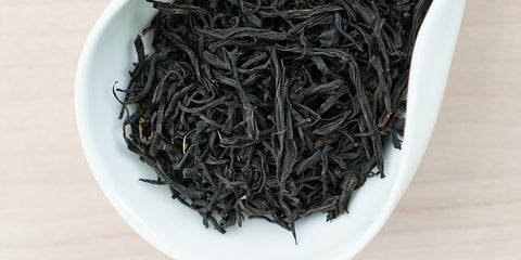 A white dish containing dry black tea leaves.