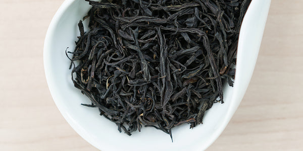 A white dish containing dry black tea leaves.