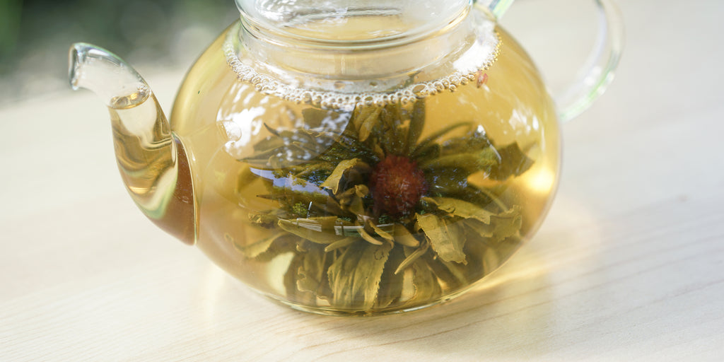 A glass teapot with a flower of tea leaves blooming inside as it brews with a pink center