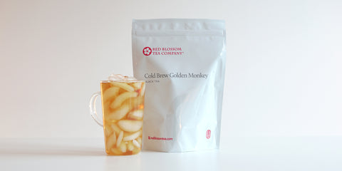 A glass cup filled with ice and black tea next to a package of Cold Brew Golden Monkey.