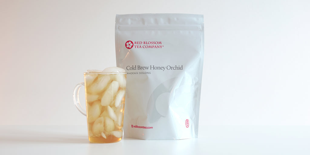A glass cup filled with ice and Phoenix oolong tea next to a package of Cold Brew Honey Orchid.