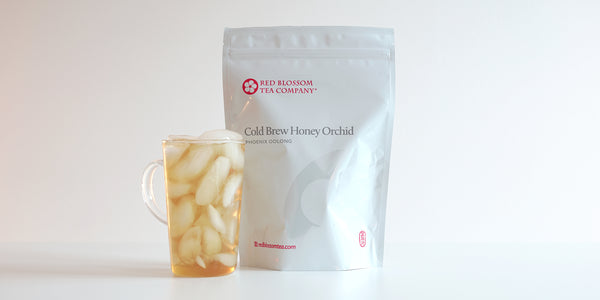 A glass cup filled with ice and Phoenix oolong tea next to a package of Cold Brew Honey Orchid.