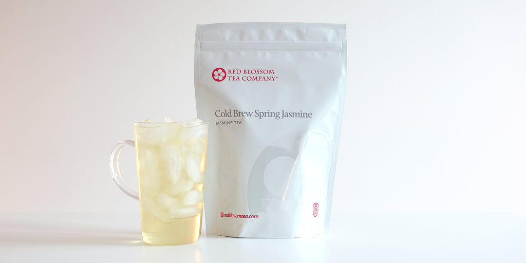 A glass cup filled with ice and jasmine tea next to a package of Cold Brew Spring Jasmine.