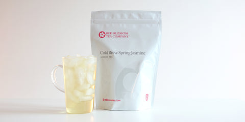 A glass cup filled with ice and jasmine tea next to a package of Cold Brew Spring Jasmine.