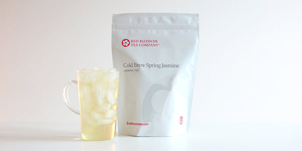 A glass cup filled with ice and jasmine tea next to a package of Cold Brew Spring Jasmine.
