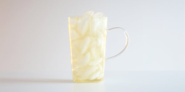 A glass cup filled with ice and jasmine tea on a white background.