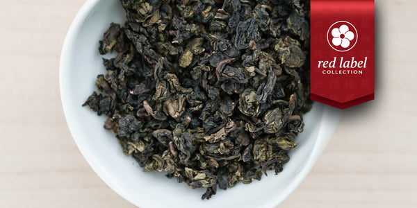 A white dish containing dry Tieguanyin tea leaves. A red ribbon in the top right corner reads “Red Label Collection”