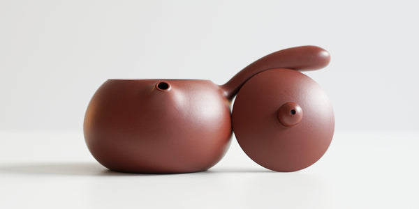 Front view of a terracotta-colored yixing teapot. The lid is facing the camera, resting against the handle.